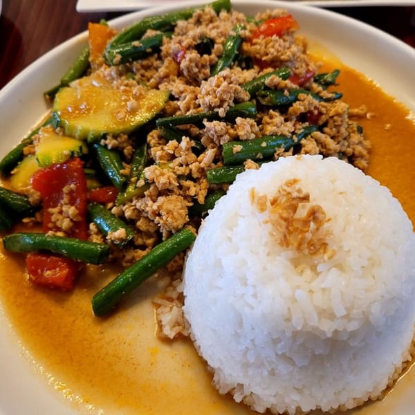 Thai basil chicken with green beans, red peppers, zucchini, and white rice on a white plate.