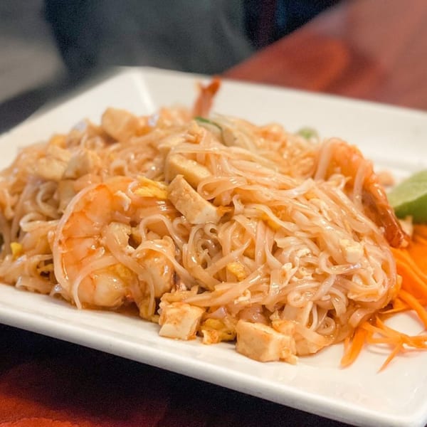 Close-up of a plate of Thai Pad See Ew noodles with shrimp, tofu, and shredded carrots.