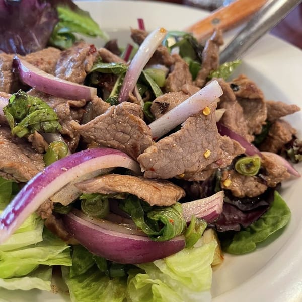 Close-up of a Thai beef salad with red onions, green lettuce, and chili flakes.
